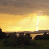 Im Vordergrund düster-grüne Landschaft mit Sträuchern und Bäumen rund um Schloss Salenstein am Untersee. Ein greller Blitz verbindet die graue Wolkendecke mit der Landschaft. Quelle: www.sturmforum.ch Fotograf: Chris Sigrist
