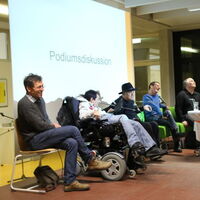 Gute Stimmung, lachende Gesichter auf dem Podium von rechts. Auf der grünen Couch sitzen Moderatorin Nadine Allgäuer, Marco Walch, Bruno Kühne und Andreas Guth. Dann zwei Rollstuhlfahrer Reinhard Zischg und Süleyman Kurt und ein Persönlicher Assistent.