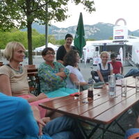 Links im Bild Nationalratsabgeordnete Helene Jarmer und Landtagsabgeordnete Vahide Aydin. Sie sitzen zusammen mit VertreterInnen von Reiz um einen großen Tisch im Freigelände der Dornbirner Messe. Der Breite Berg winkt aus der Ferne.