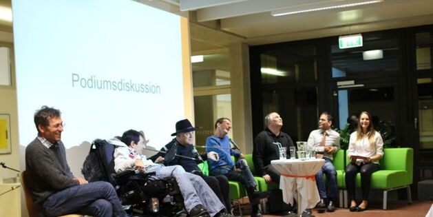 Gute Stimmung, lachende Gesichter auf dem Podium von rechts. Auf der grünen Couch sitzen Moderatorin Nadine Allgäuer, Marco Walch, Bruno Kühne und Andreas Guth. Dann zwei Rollstuhlfahrer Reinhard Zischg und Süleyman Kurt und ein Persönlicher Assistent.