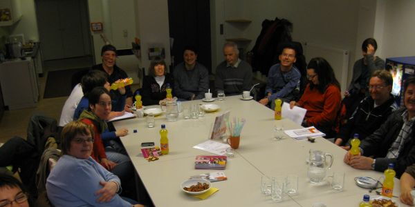 Viele Menschen sitzen um einen großen Tisch und lachen in die Kamera