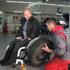 Reifenwechsel: Eine junge Frau im Rollstuhl schaut dem Automechaniker zu, der versucht einen Autoreifen auf ihrem Rollstuhl zu montieren.
