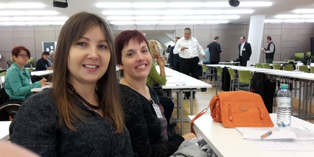 Elisabeth und Julia beim ÖAR-Tag in Wien. Tasche, Trinkflasche und Schreibmaterial auf dem Tisch. Im Hintergrund andere SeminarteilnehmerInnen in Erwartung des Eröffnungsreferates mit und ohne Blick aufs Handy.