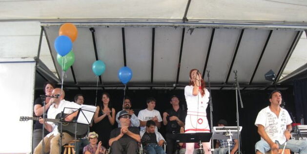 Die Band C.C.Mate mit VertreterInnen des Vorarlberger Krüppelkabaretts auf der Bühne. Bunte Ballone schmücken den linken Rand der Bühne.