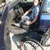 Benjamin Tschugmell am Steuer seines blauen Autos. Sein Rollstuhl wartet auf seinen Platz am Beifahrersitz.