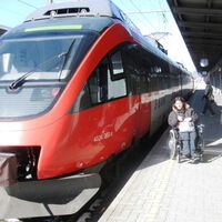 Ein Niederflurzug am Bahnsteig 1 in Bludenz. Claudia Fessler und Sueleyman Kurt warten in ihren Elektrorollstühlen auf dem Bahnsteig auf den Einstieg.