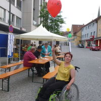 Julia Fischbach, junge hübsche Frau mit rötlichen Haaren, schaut fröhlich in die Kamera. Sie hält einen rot leuchtenden Luftballon mit Postkarte startbereit in die Höhe.
