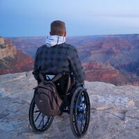 Ein Rollstuhlfahrer steht auf einem Felsplateau mit weitem Blick auf den Grand Canyon. Fotoquelle: www.freeonwheels.de