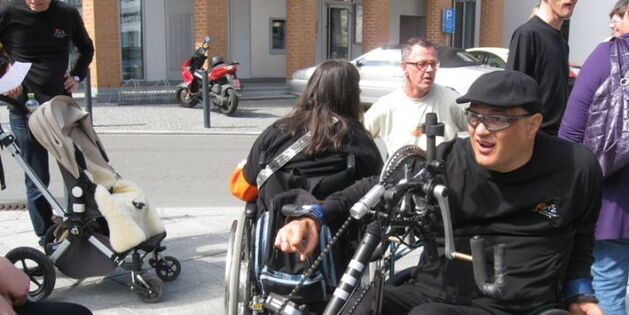 Ein Rollstuhlfahrer in seinem Bike. Schwarzes Outfit und Fahrradbrille. Blick in Aufbruchstimmung und Fahrtrichtung, eine Hand am Tretlenker, bereit zur Abfahrt.