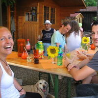 Lachende Frauen und Männer sitzen an Biertischen. Durstlöscher stehen bereit zur Kühlung. Sonnenblumendekoration. Unter einem Tisch lacht ein Hund in die Kamera.