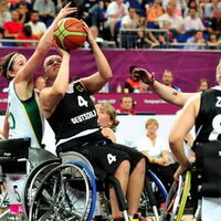 Basketballerinnen in Rollstühlen beim Spiel. Eine Frau versucht den Ball Richtung Korb zu werfen. Die Gegenspielerin im weißen Dress hält dagegen. Im Hintergrund Teammates und Zuschauerränge. Foto: backview.eu, Andreas Joneck