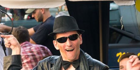 Foto: Ralph Hoppe. Schwarzer Ledermantel, schwarzer Schal, schwarze Fliege, schwarze Brille, schwarzer Hut. Ein fröhliches Lächeln - Hände zum Tanz ausgebreitet, Andi Guth alias Mister Bonspastik tanzt durch das Publikum.