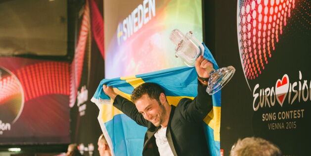Der Sieger des Songcontest 2015 Mans Zermerlöw hält die Schwedische Flagge und das gläserne Mikrofon in die Höhe und posiert für die Fotografen und das Publikum. (Fotoquelle: www.eurovision-austria.com)