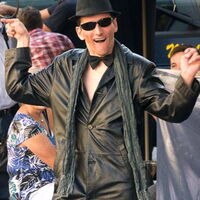 Foto: Ralph Hoppe. Schwarzer Ledermantel, schwarzer Schal, schwarze Fliege, schwarze Brille, schwarzer Hut. Ein fröhliches Lächeln - Hände zum Tanz ausgebreitet, Andi Guth alias Mister Bonspastik tanzt durch das Publikum.