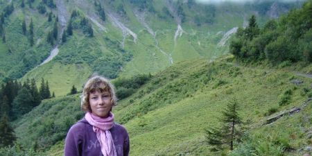 Ein Mädchen hält einen Esel am Zügel. Im Hintergrund Almweide mit Wald.