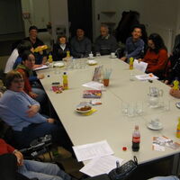Viele Menschen sitzen um einen großen Tisch und lachen in die Kamera.