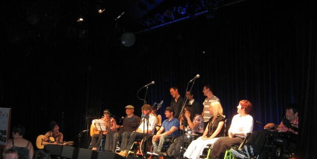 Der Reiz-Krüppelchor auf der Bühne im Freudenhaus. Acht RollstuhlfahrerInnen mit drei Spastikern. Ganz links an der Gitarre: Philipp Lingg von der Formation holstounarmusigbigbandclub.