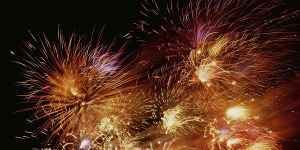 Vor nächtlichem schwarzem Hintergrund leuchtende Feuerwerkskörper. Als ob viele Lichter wie helle Haare aus verschiedenen kleinen Sonnenzentren ausstrahlen.