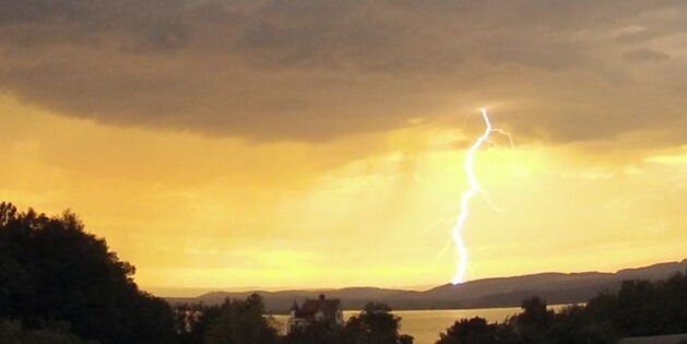 Im Vordergrund düster-grüne Landschaft mit Sträuchern und Bäumen rund um Schloss Salenstein am Untersee. Ein greller Blitz verbindet die graue Wolkendecke mit der Landschaft. Quelle: www.sturmforum.ch Fotograf: Chris Sigrist