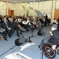 Foto: VLK/A. Serra. Rechts im Vordergrund singt Reinhard Zischg das Siegerlied, begleitet von Matthias Zabransky an der Gitarre. Im Hintergrund das Publikum bei der Chancenpreisverleihung 2011. Ein vollbesetzter Montfortsaal.