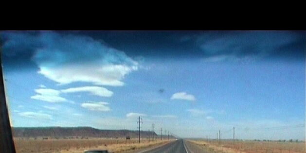 Blick aus dem Auto: Blauer Himmel mit spärlichen Wolken. Sand, kaum Pflanzen. Eine lange gerade Straße verschwindet am Horizont. Ein Pickup kommt entgegen, sonst ist die Straße frei.