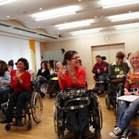 Foto: Bizeps. Gute Stimmung bei den KongressteilnehmerInnen. Viele lachende Gesichter und applaudierende Hände. Im Vordergrund Claudia Fessler und Sabrina Nitz in ihren Rollstühlen.