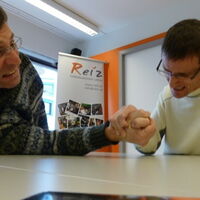 Zwei Männer beim Armdrücken. Die Hand des Mannes links berührt fast schon den Tisch. Sein Blick eine verzweifelte Grimasse. Der Mann rechts hat gleich gewonnen. Verbissen grimmig versucht er die Hand des Gegners auf den Tisch zu drücken.